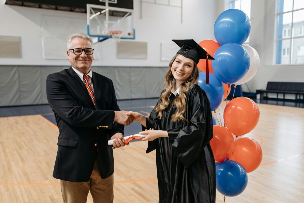 A proud graduate receiving a diploma from a teacher during a ceremony in a gymnasium.